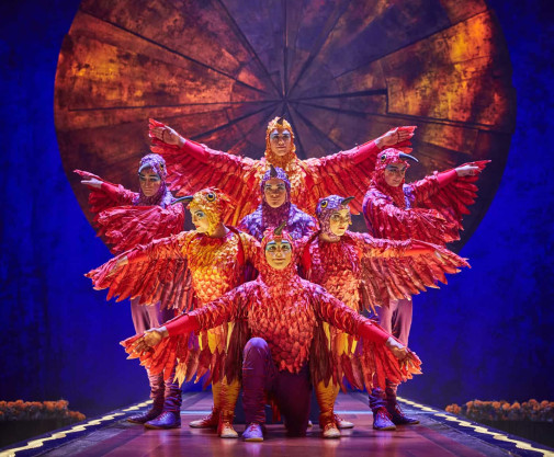 Performers in red avian costumes pose in symmetrical layered formation.