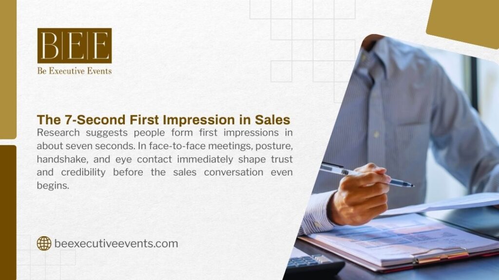 Business professional in light shirt giving firm handshake during face-to-face sales meeting, emphasizing posture, eye contact, and 7-second first impression at desk with notes and pen.